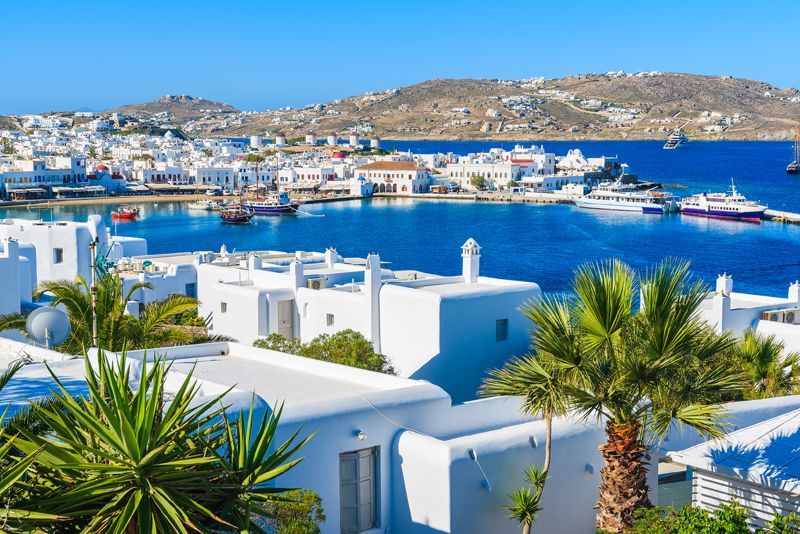 A city with a lot of white buildings and palm trees in front of a body of water.