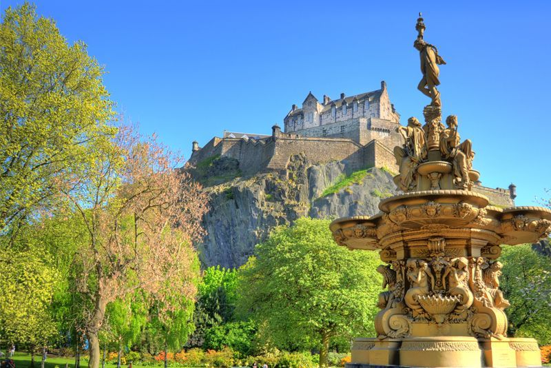 A fountain in a park with a castle in the background.