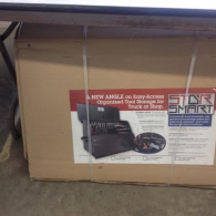 A cardboard shipping box containing a StorSmart brand angle-style tool storage unit for a truck or shop.