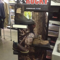 A Rocky-branded retail display featuring three styles of brown leather work and hunting boots on tiered shelves.