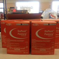 Several orange boxes of DuPont Pastora herbicide lined up on a counter in a retail setting.