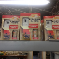 Three identical boxes of Flying Insect Kill System dispensers with aerosol refills displayed on a store shelf.