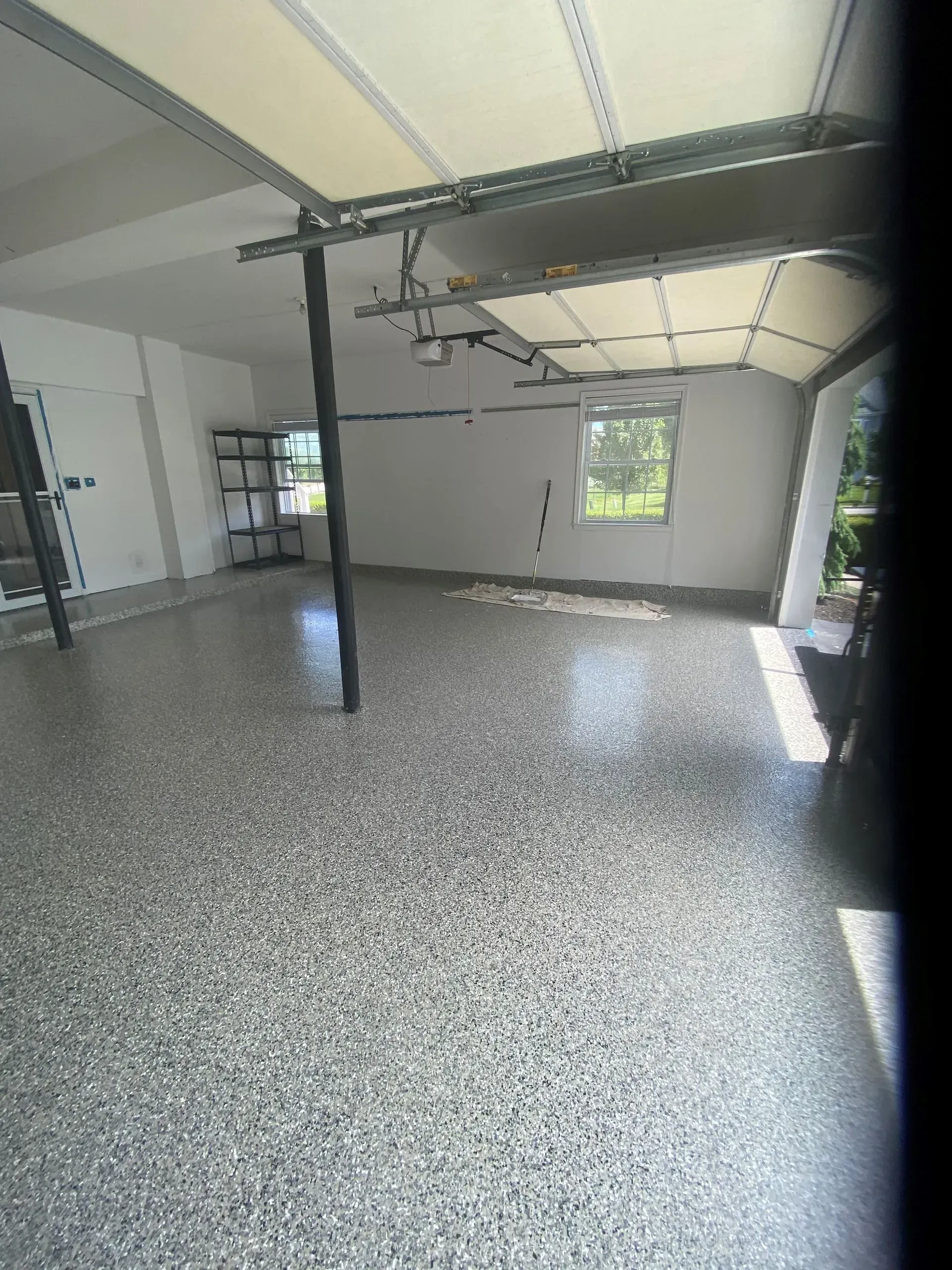Empty garage with speckled grey floor, white walls, and open garage door.