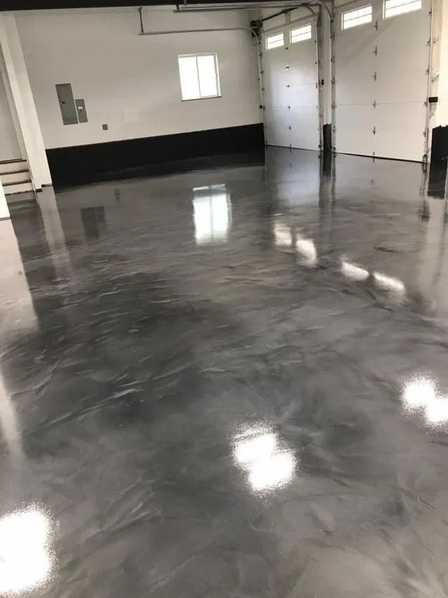Shiny, metallic gray epoxy floor in a garage with closed white doors and a small window.