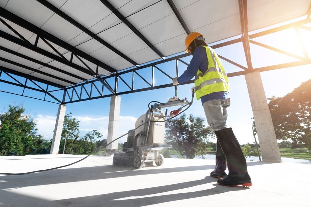 Person in safety gear using a concrete grinder inside a building, sunny day.