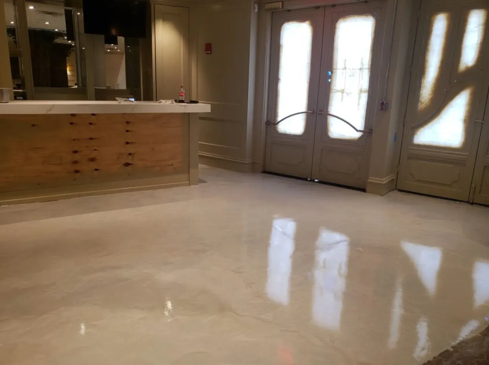 A shiny, light-colored floor reflects the light from a doorway. A wooden bar is to the left.