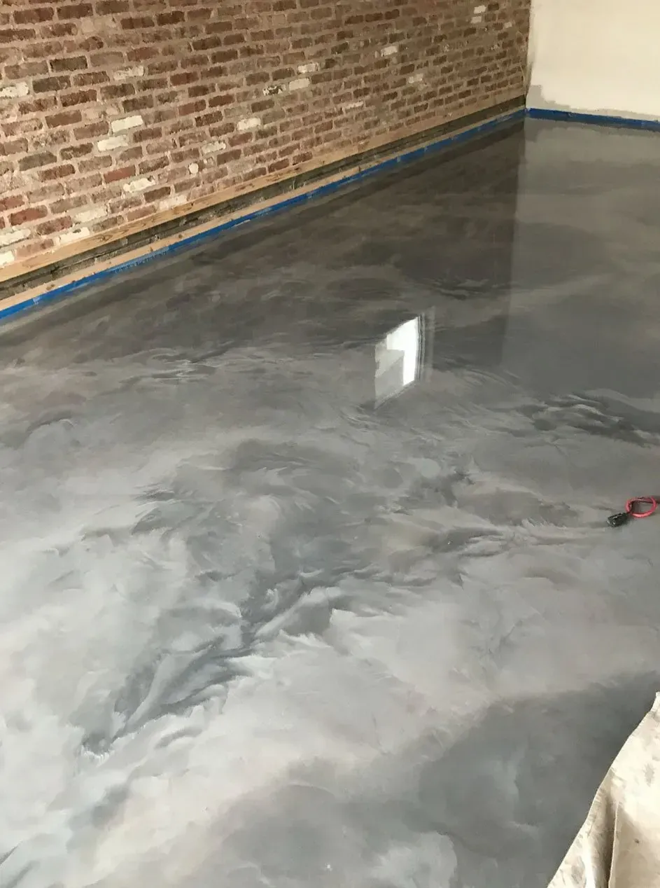 Grey metallic epoxy floor in a room with a brick wall.