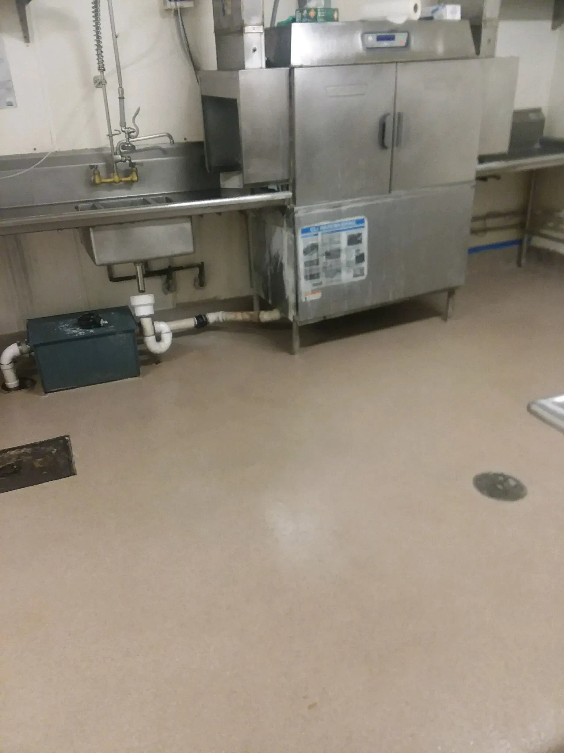 A commercial kitchen with a stainless steel dishwasher, sink, and beige floor.