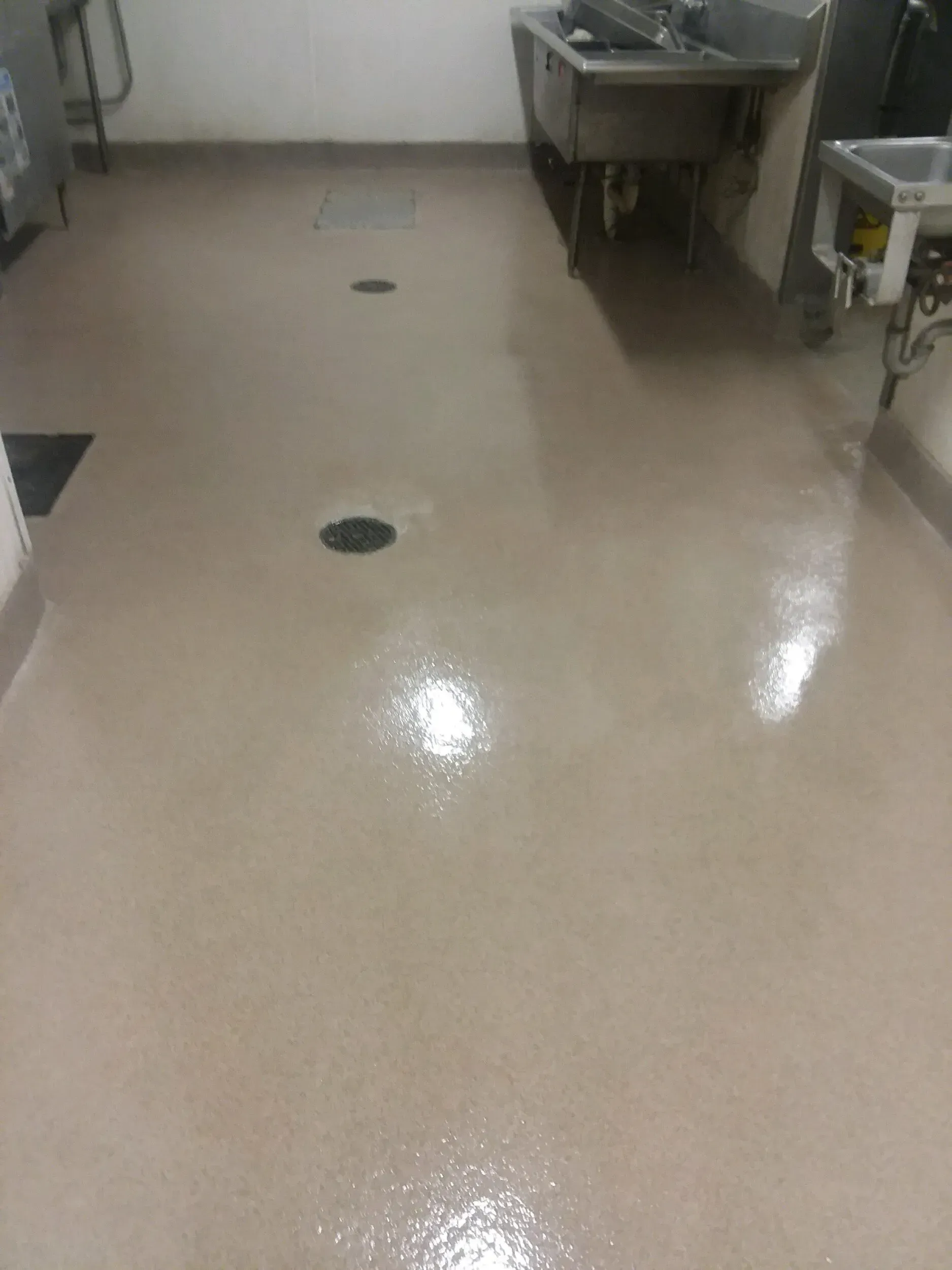 Beige, glossy commercial kitchen floor with three round floor drains, a sink, and countertops.