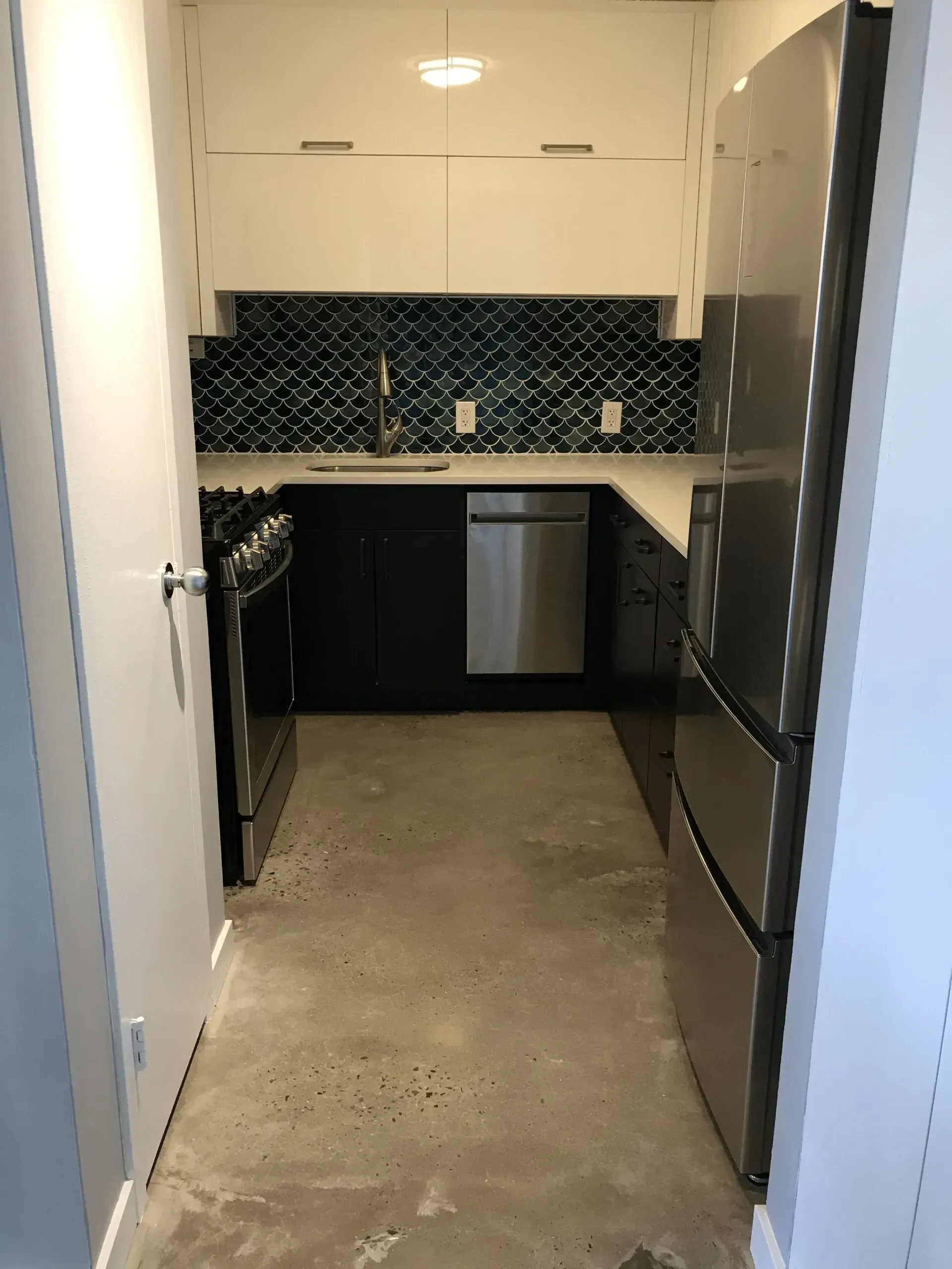 Small modern kitchen with stainless steel appliances, dark cabinets, and blue tile backsplash.