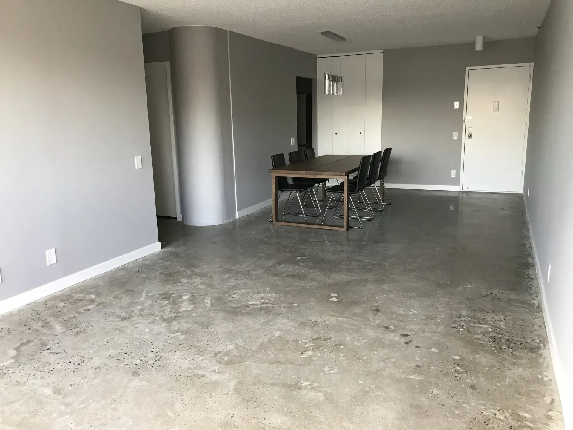Empty room with concrete floor, gray walls, dining table with chairs, and white doors.