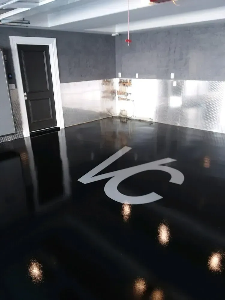 Glossy black garage floor with a white logo; stainless steel wall accents.