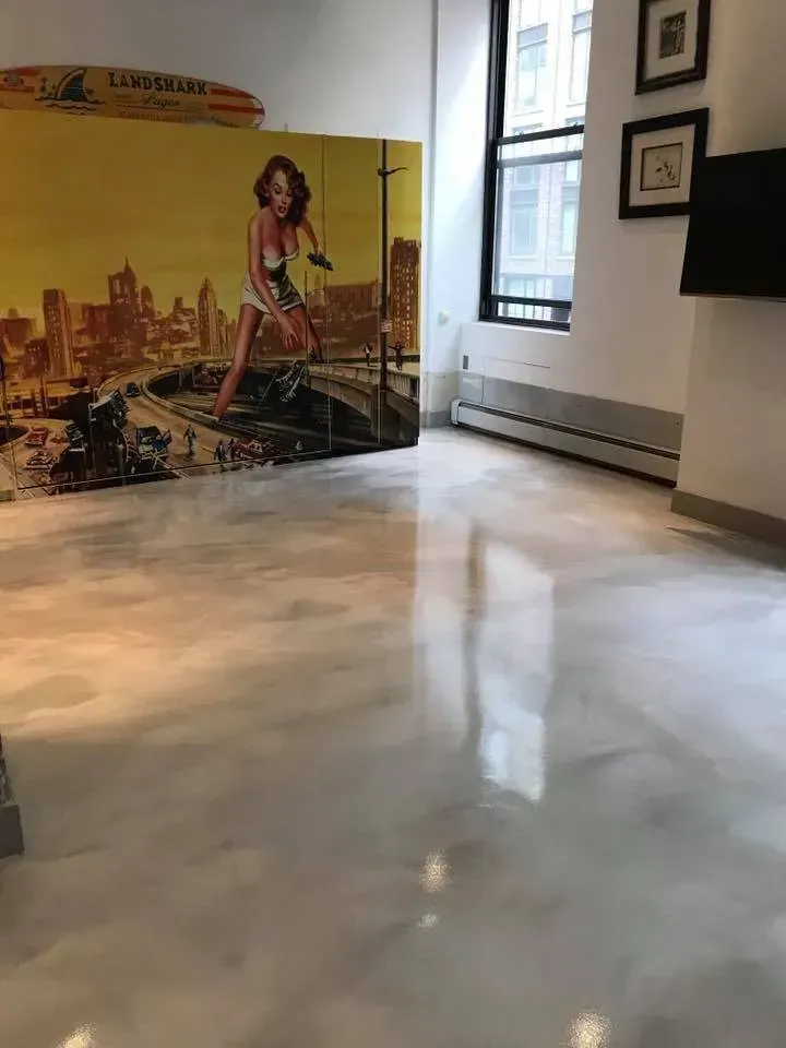 Shiny, light gray epoxy floor in a room, with a large art piece on the wall and a window.