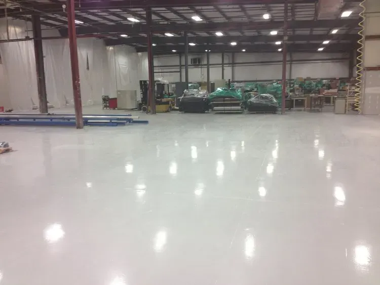 Bright white, glossy industrial warehouse floor with machinery and ceiling lights.
