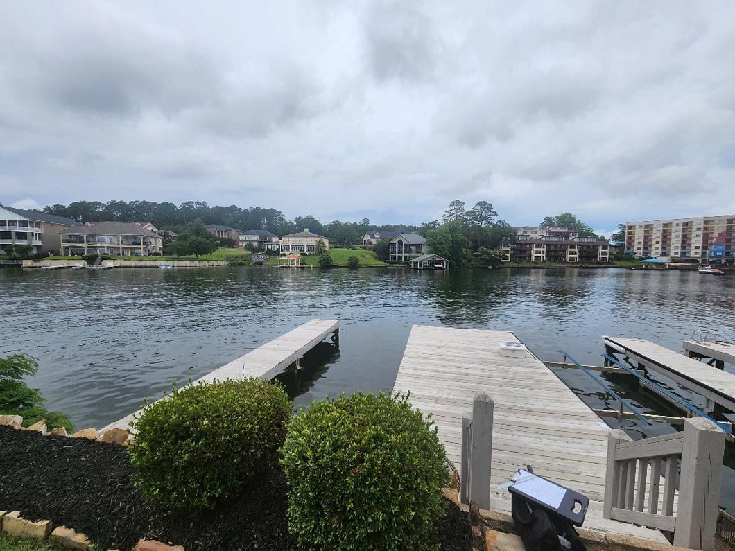 A view of a lake with a dock in the foreground and houses in the background.