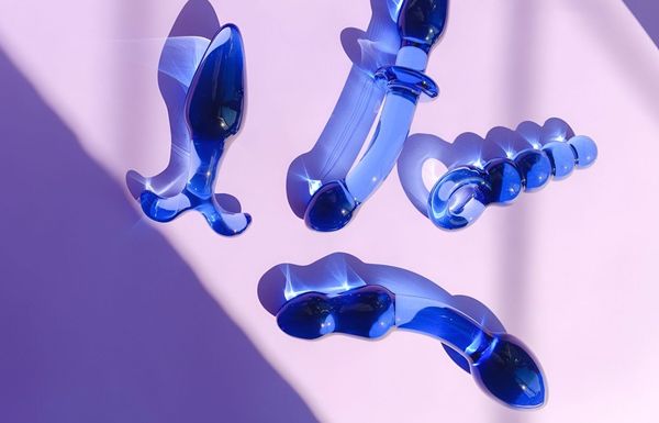 Tres juguetes de vidrio azul están sobre una superficie rosa.
