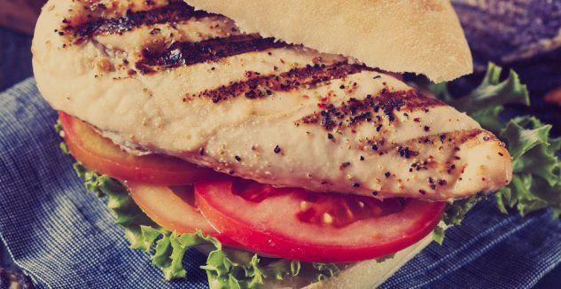 A close up of a grilled chicken sandwich with lettuce and tomatoes on a napkin.