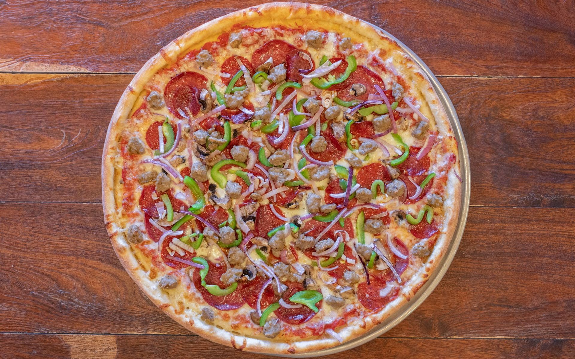 A pizza with pepperoni , sausage , green peppers , onions and cheese on a wooden table.