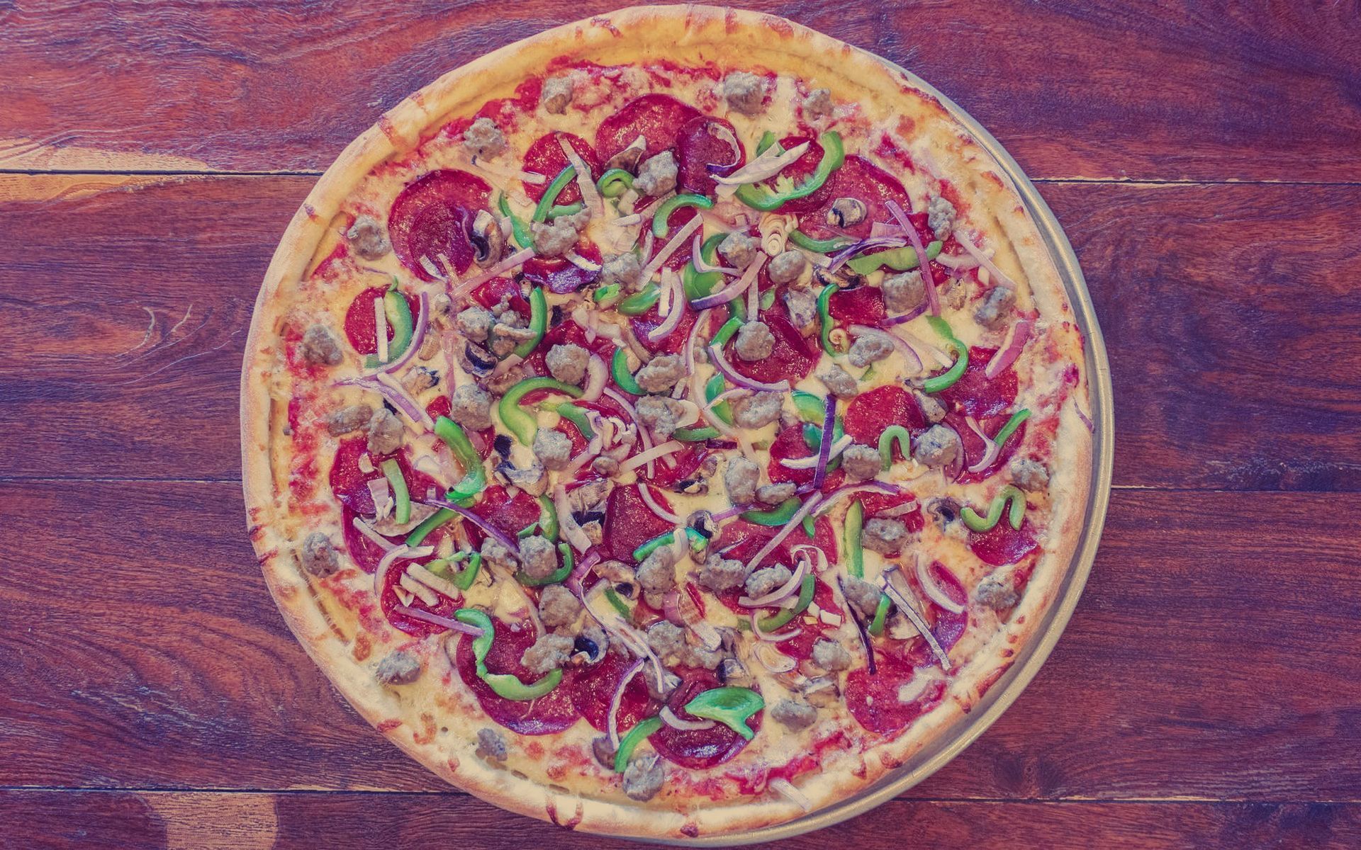 A pizza with pepperoni , sausage , green peppers , onions and cheese on a wooden table.