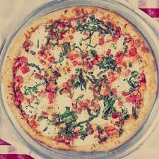A pizza with tomatoes , cheese and basil on a pan on a table.