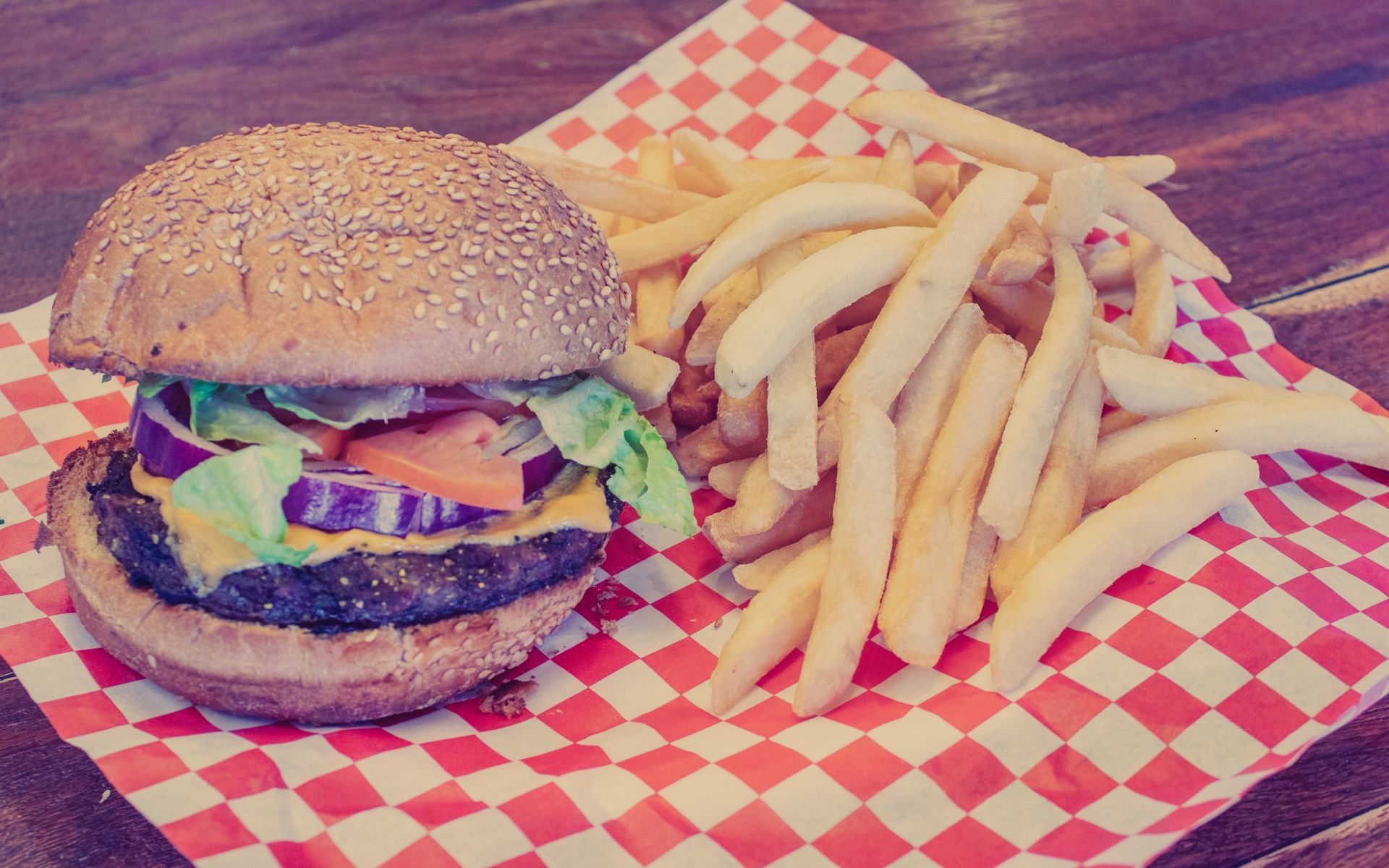 A hamburger and french fries on a checkered paper on a table.