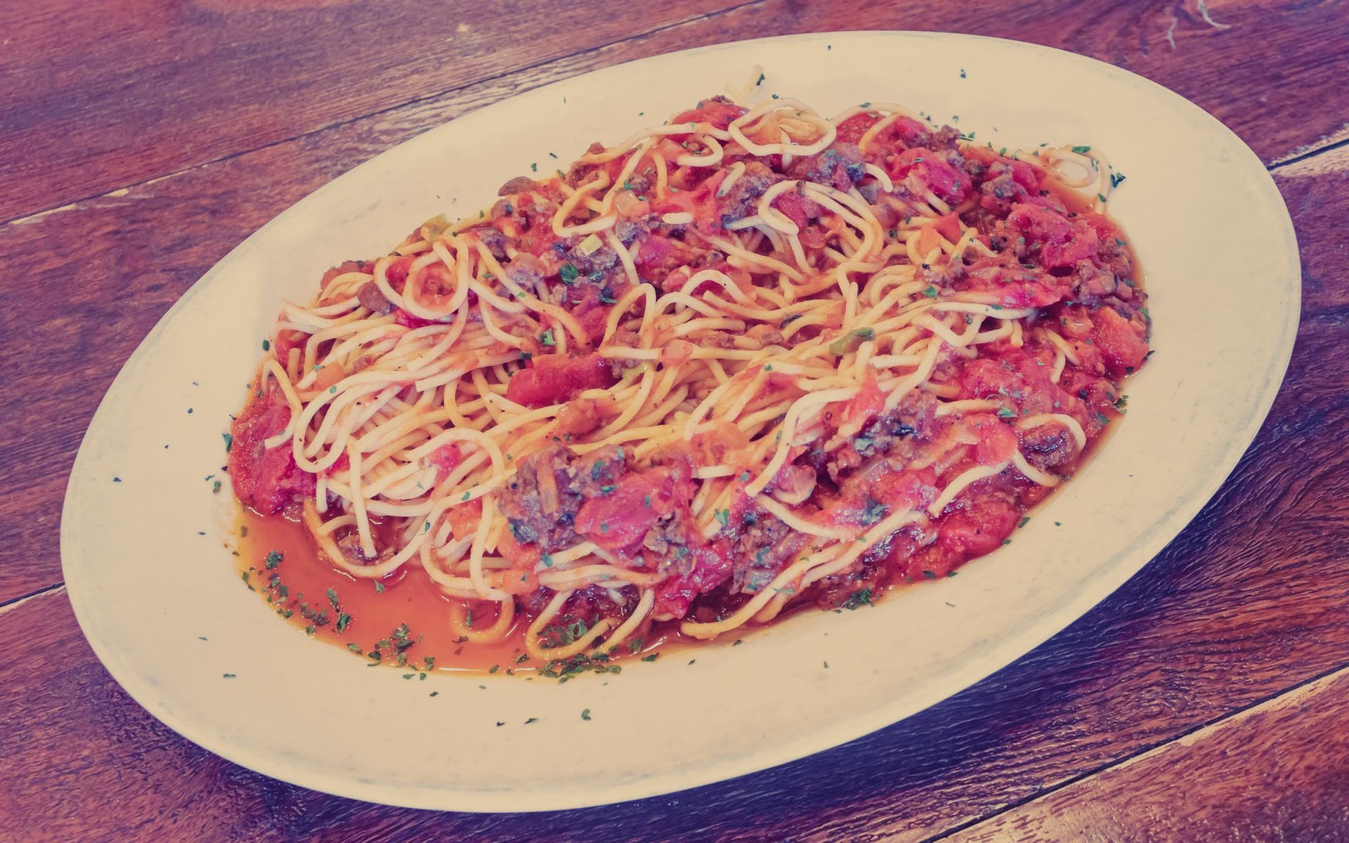 A white plate topped with spaghetti and sauce on a wooden table