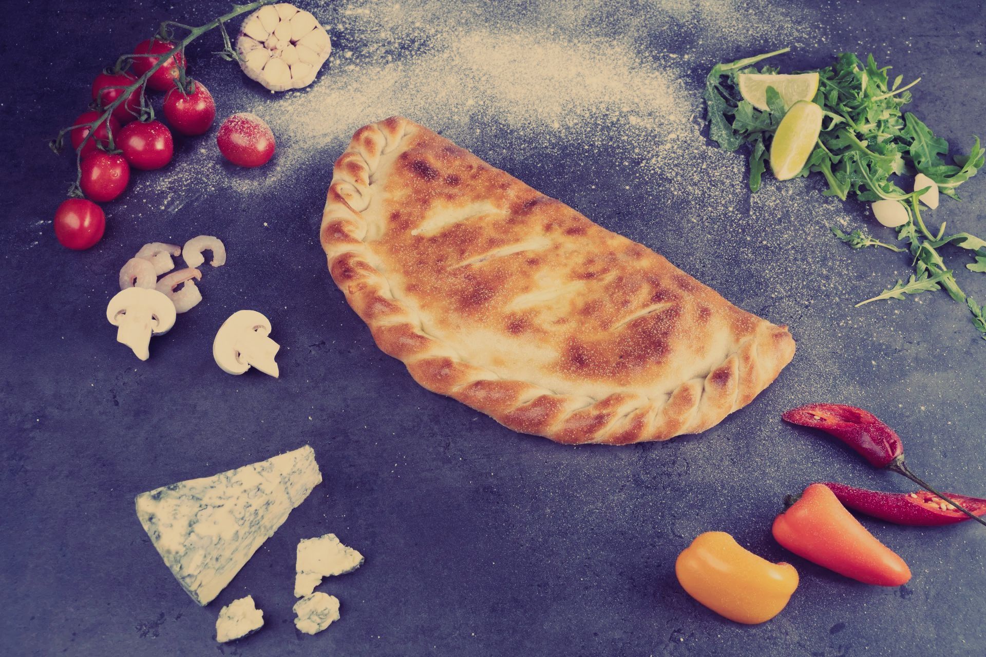A calzone is surrounded by vegetables on a table