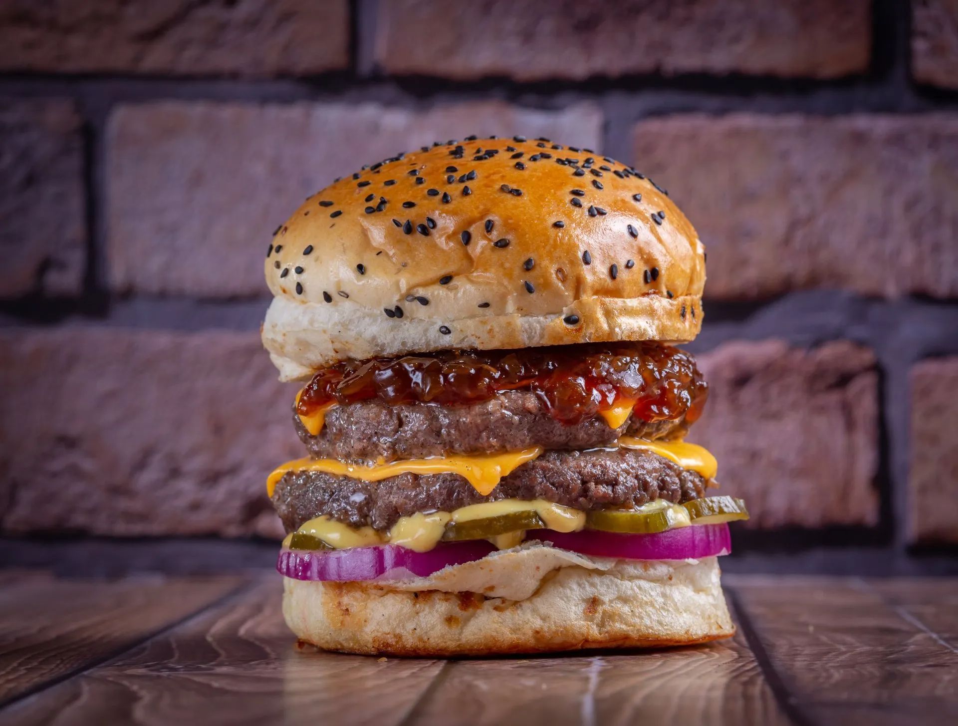 A hamburger is sitting on a wooden table in front of a brick wall.