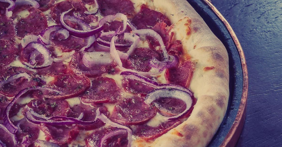A pizza with pepperoni and onions on it is sitting on a table.