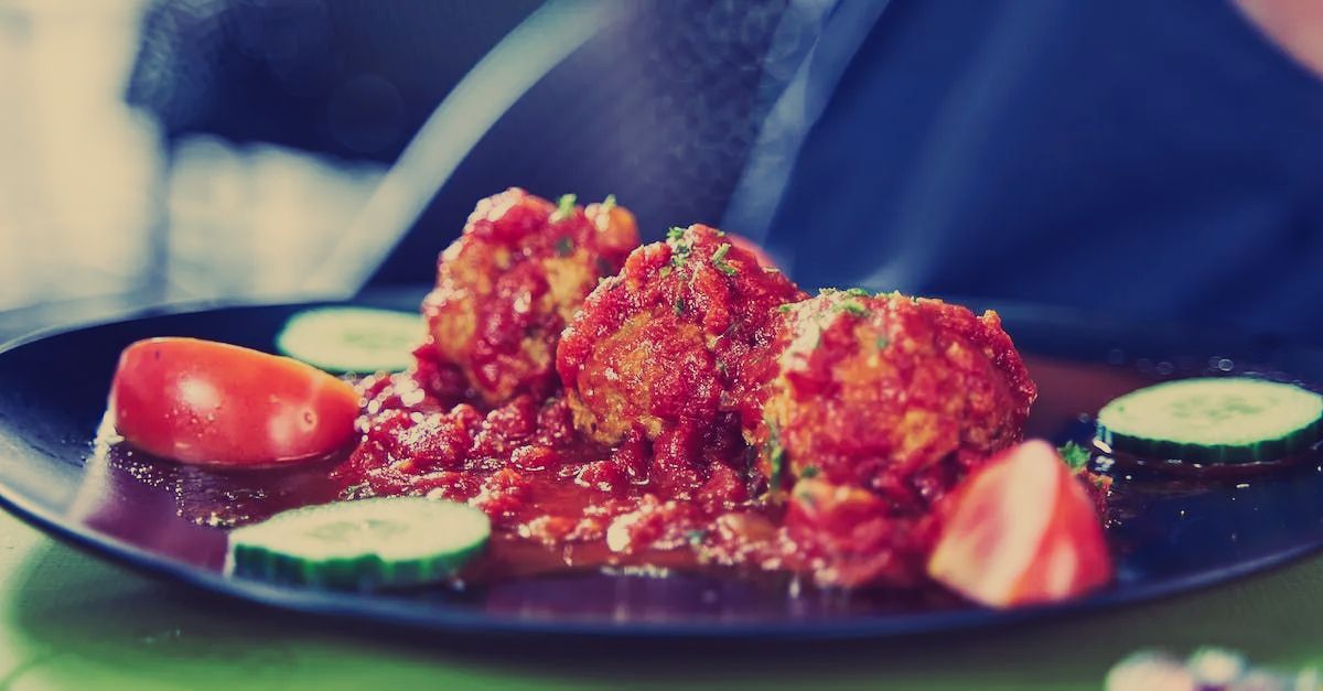 A plate of food with meatballs , tomatoes and cucumbers on a table.