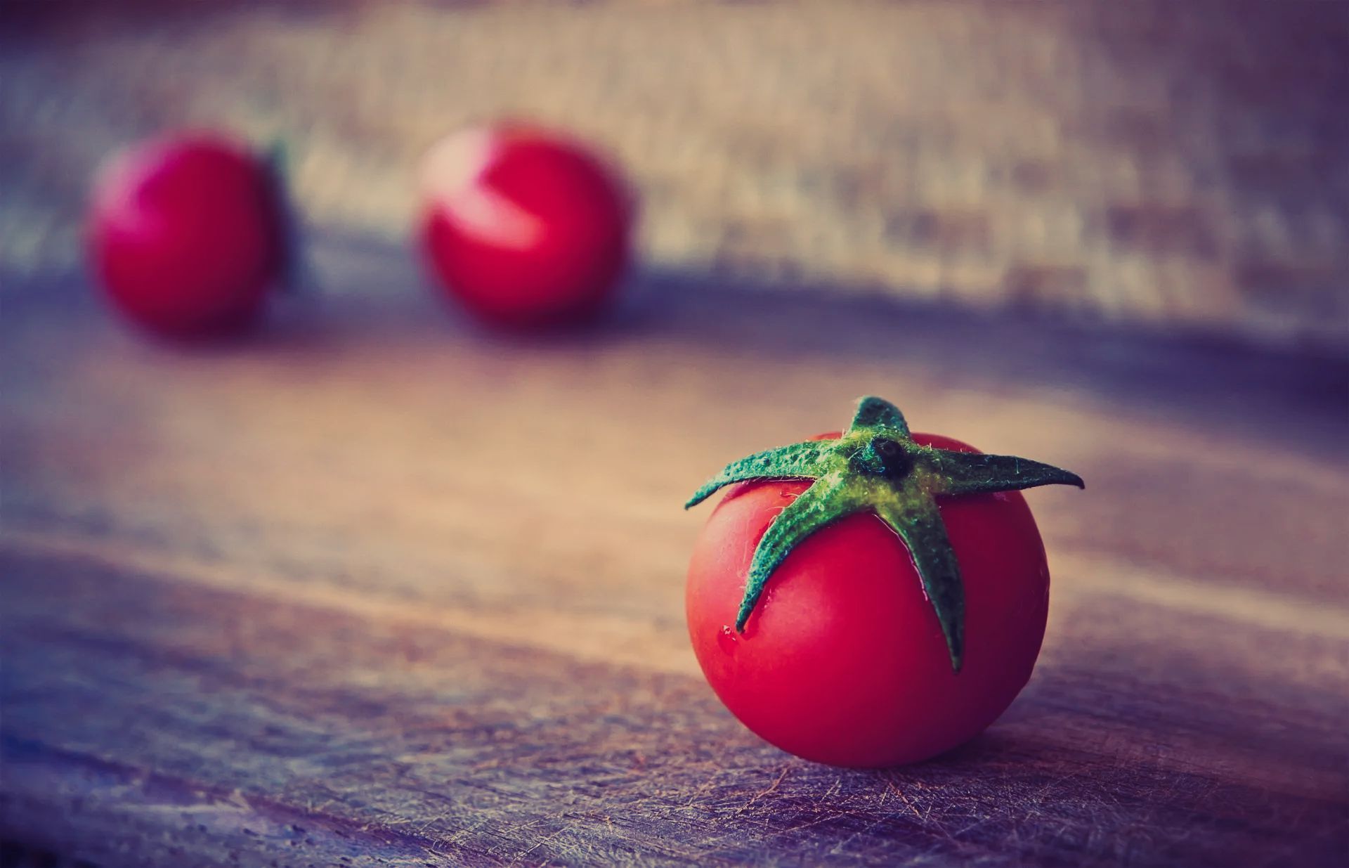 Three tomatoes are sitting on a wooden table.