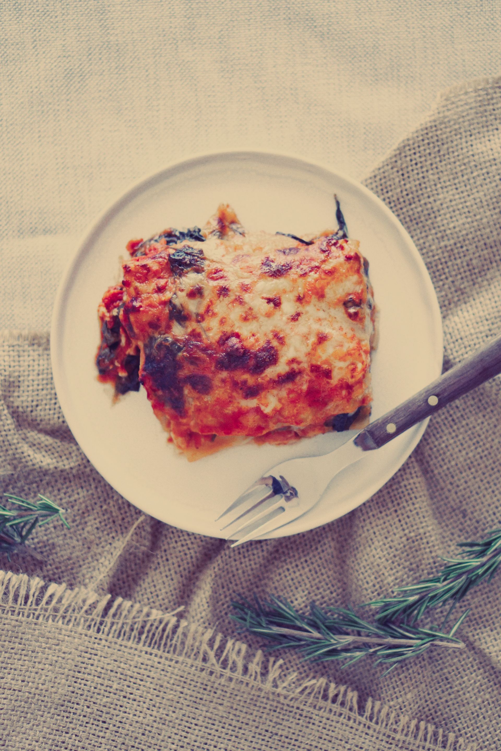 A white plate topped with a piece of lasagna and a fork