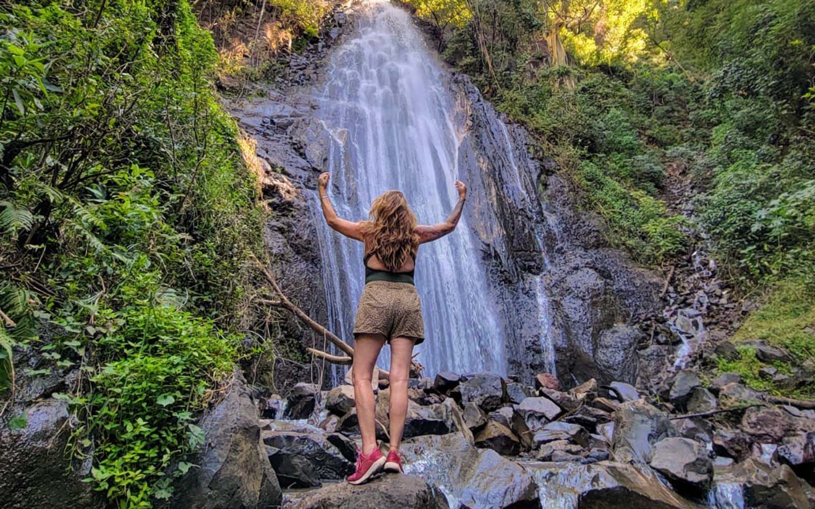 Una mujer está parada sobre una roca frente a una cascada.