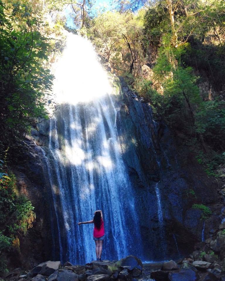 Una mujer con un vestido rojo está parada frente a una cascada.
