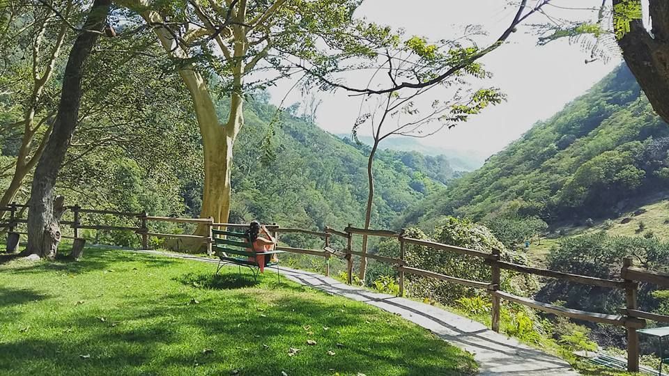 Una persona está sentada en un banco en un parque con vistas a un valle.