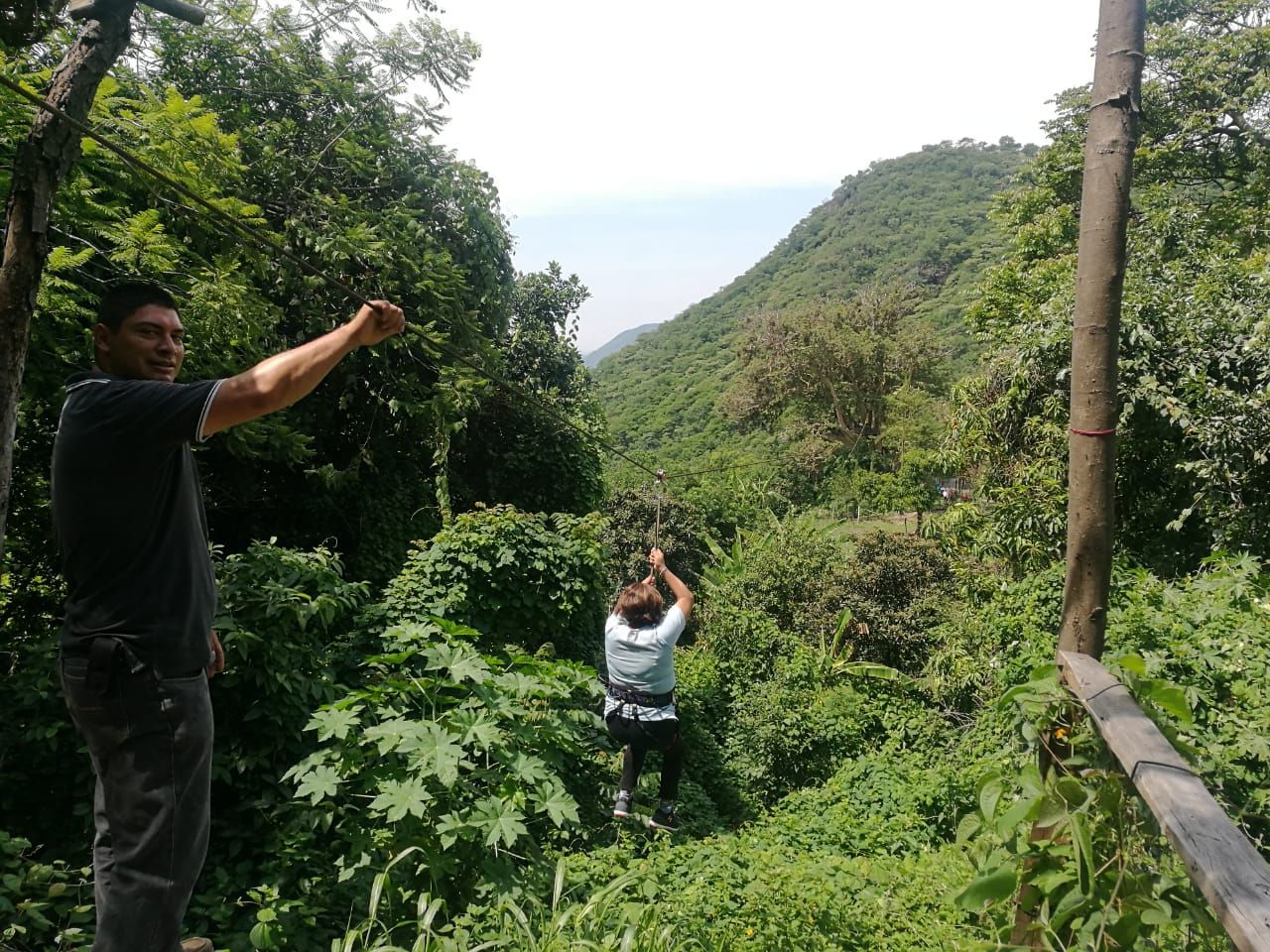 Un hombre está parado junto a una persona en una tirolina en el bosque.