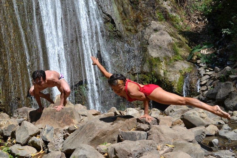 Un hombre y una mujer están haciendo yoga frente a una cascada.