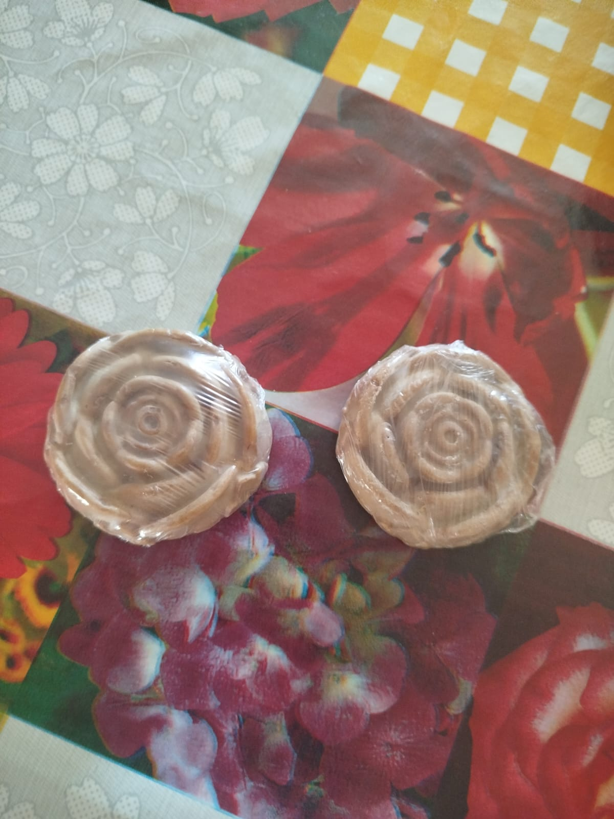 Dos jabones marrones en forma de rosa sobre un mantel floral colorido.