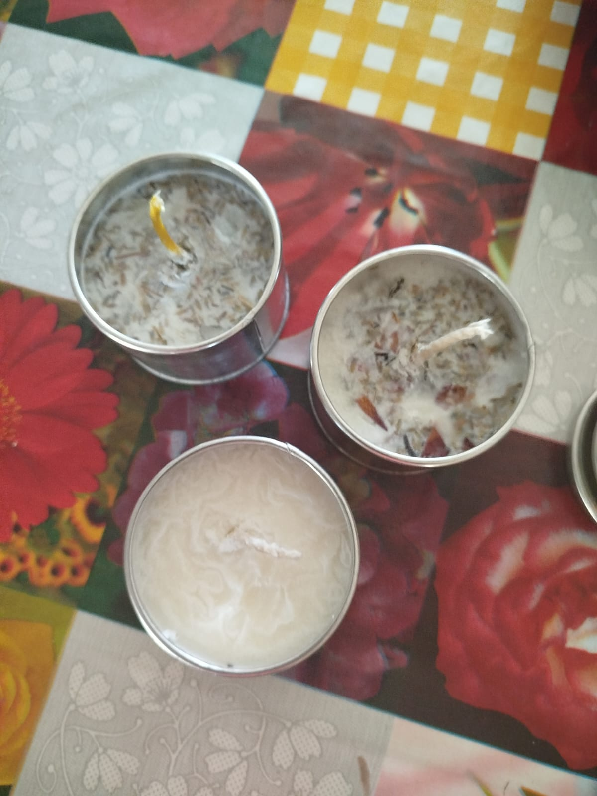 Tres velas de té encendidas con detalles florales sobre una superficie estampada de colores.