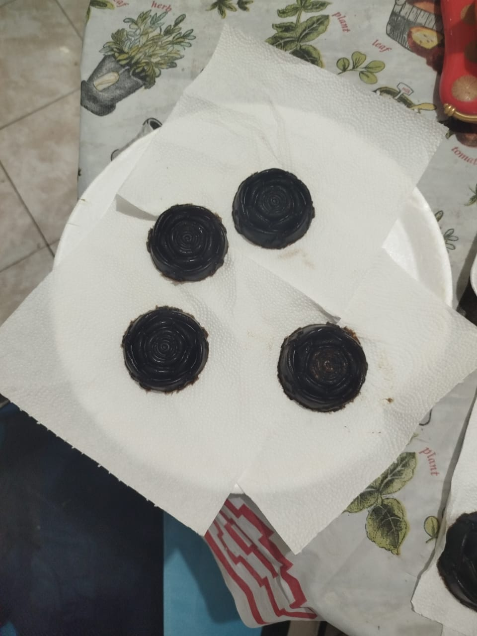 Cuatro golosinas oscuras y redondas sobre una toalla de papel blanca encima de un plato blanco.