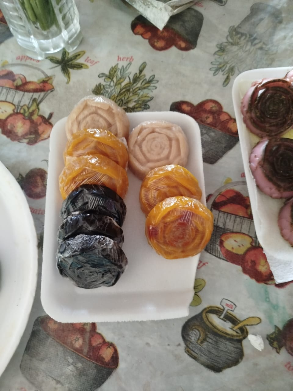 Una bandeja blanca contiene frutas secas y dulces en forma de rosa sobre un mantel floral.