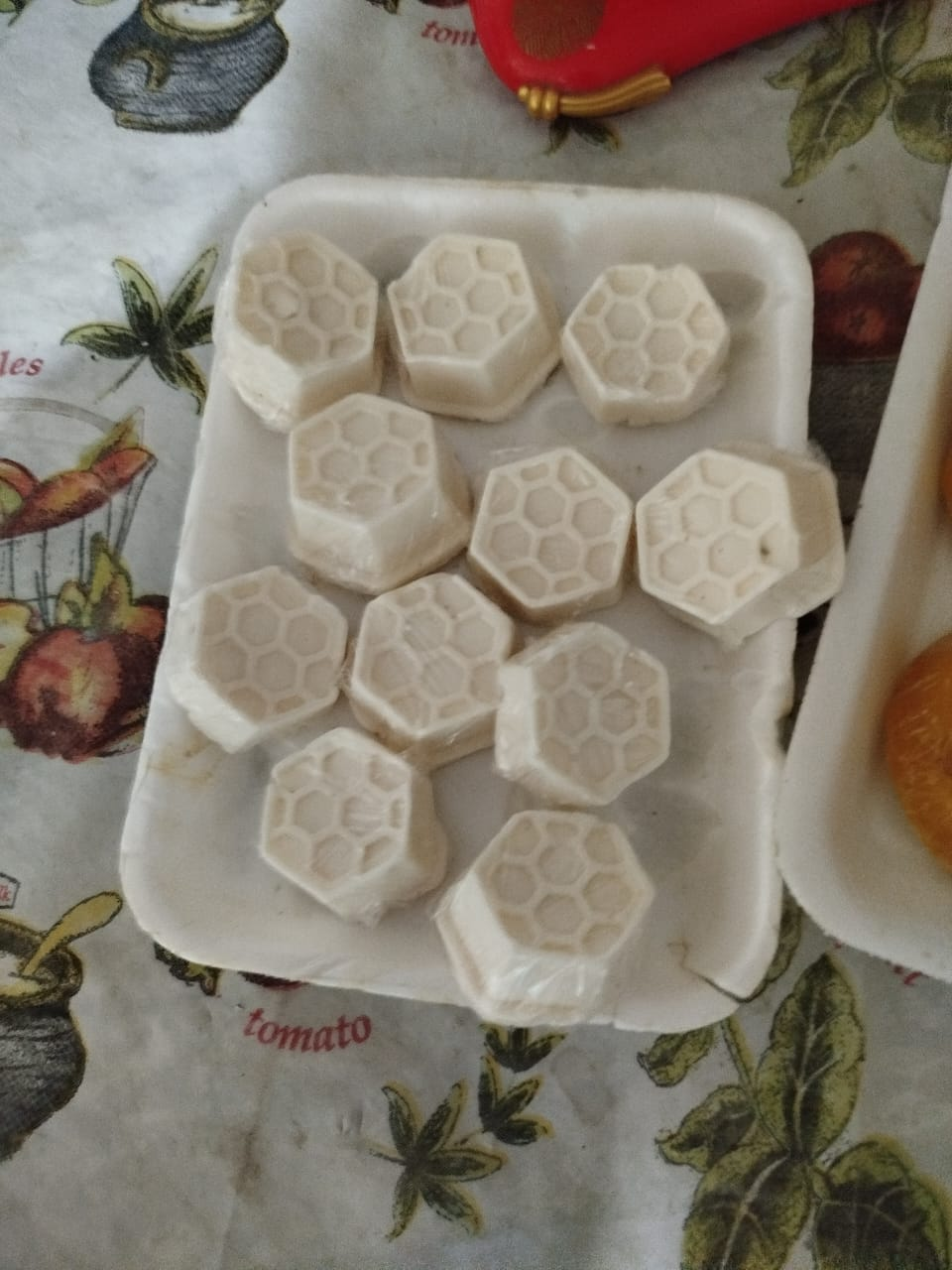 Jabones con forma de panal en un recipiente de poliestireno, sobre un mantel con motivos florales y frutales.