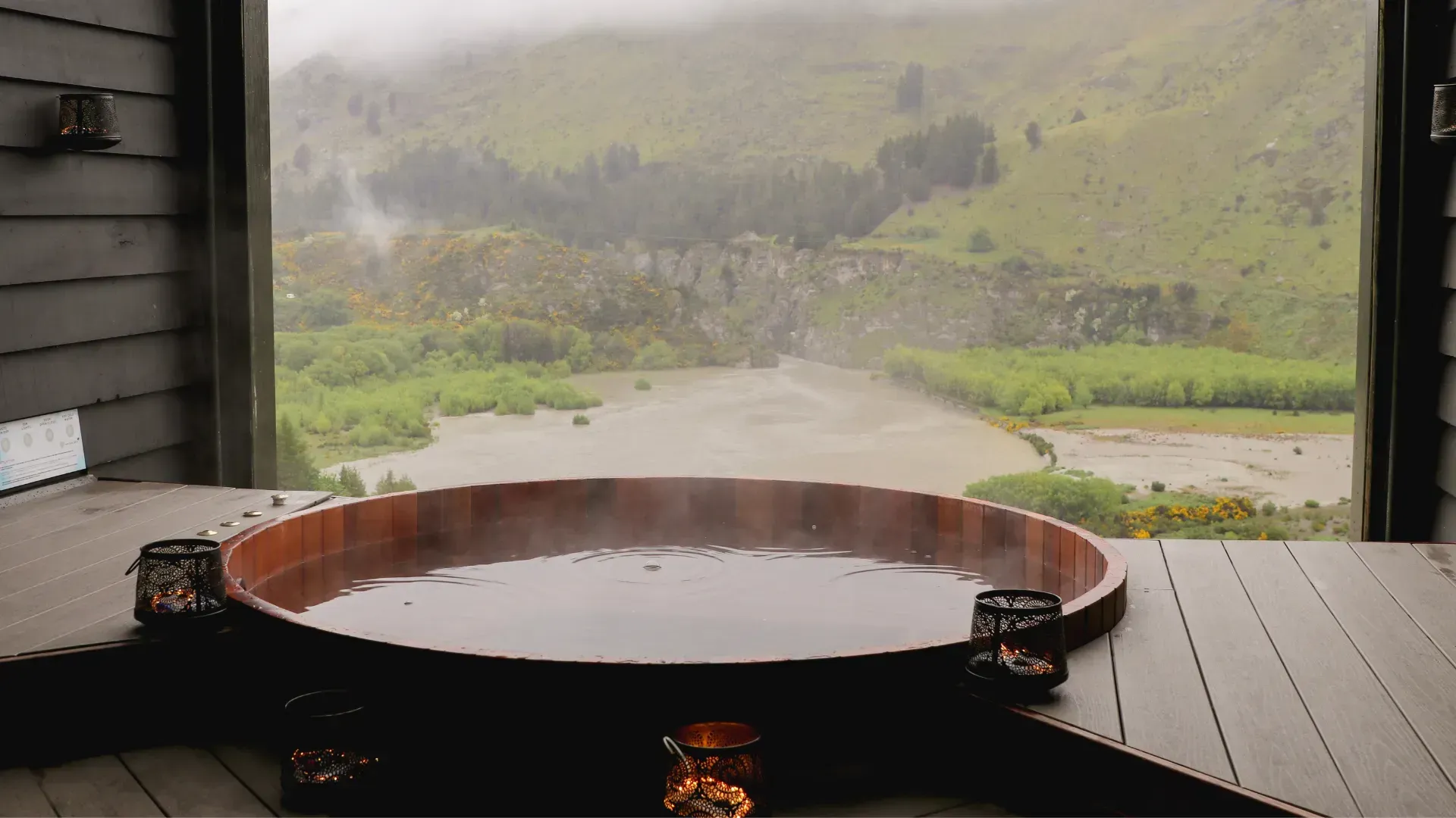 Hot tub overlooking a river and green landscape on a misty day.