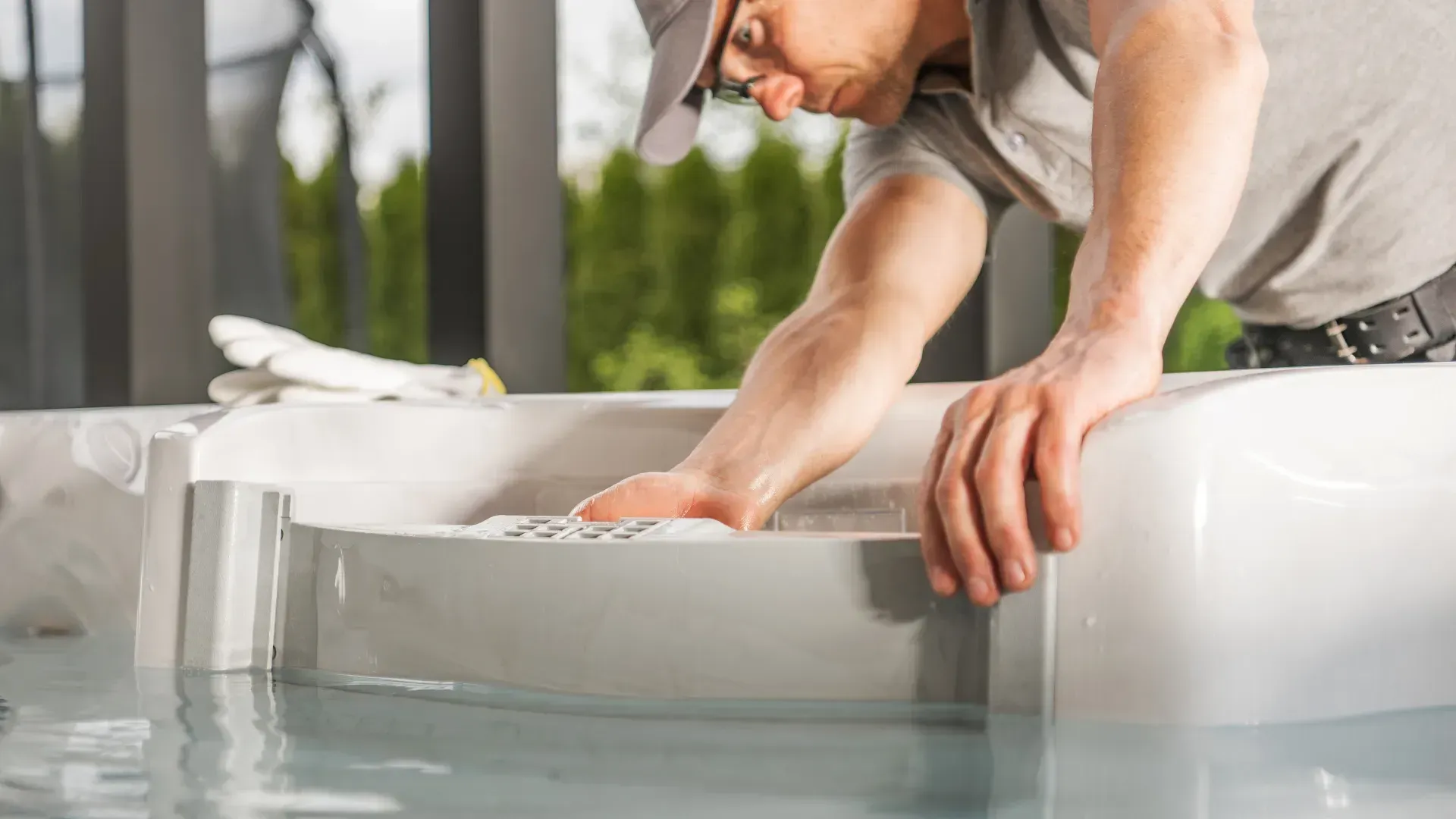 Man in cap working on a white hot tub, outdoors.