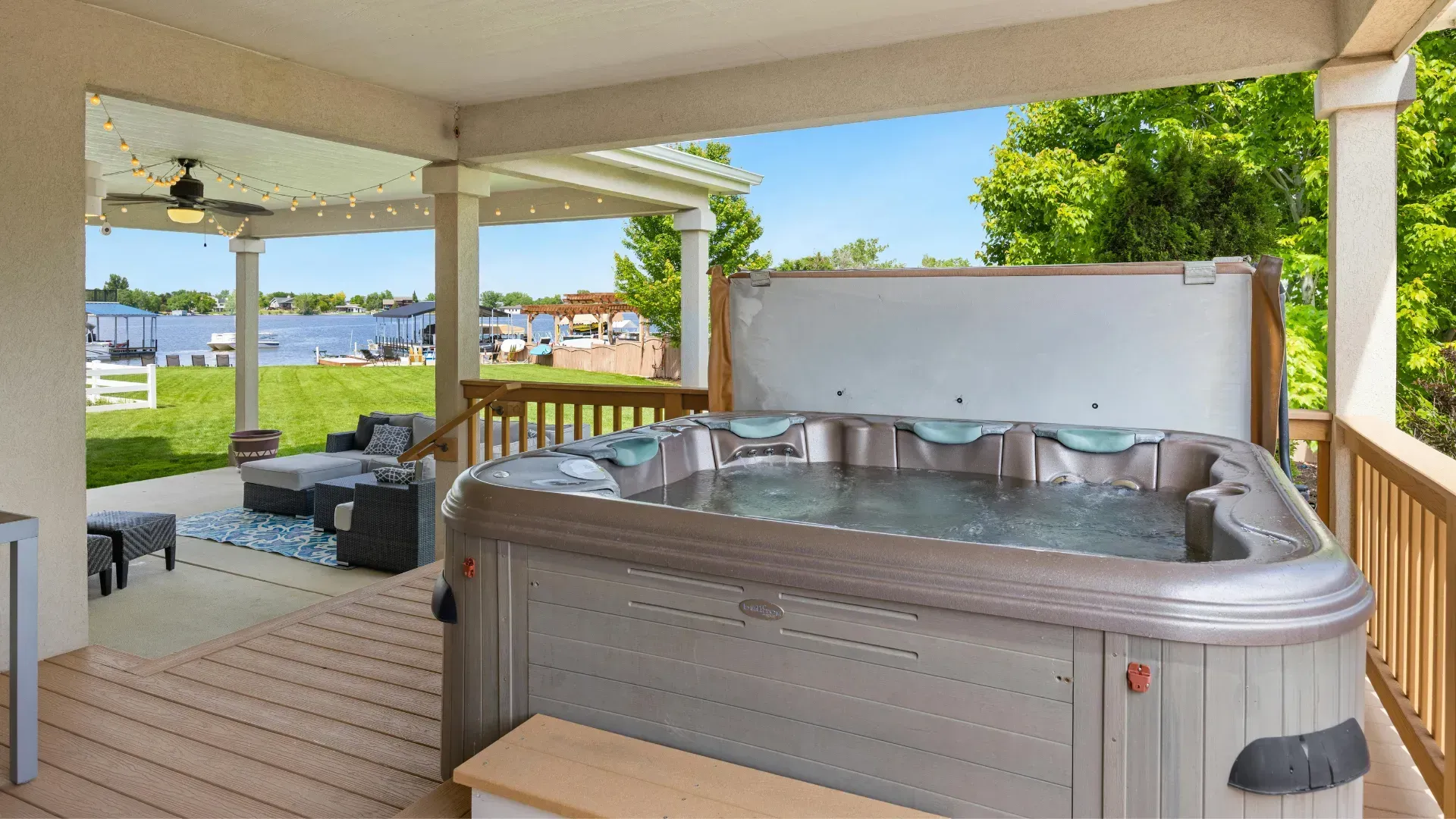 Hot tub on a wooden deck, overlooking a lake, under a covered patio.