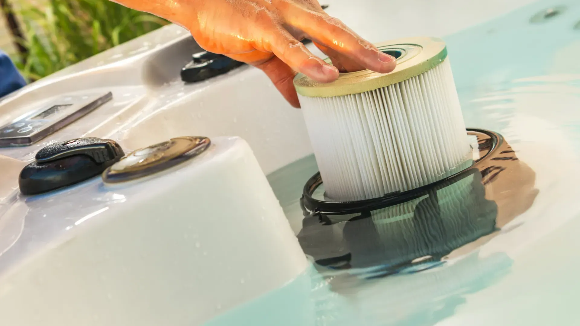 Person placing a filter into a hot tub. Close-up of white hot tub with blue water and a person's hand.