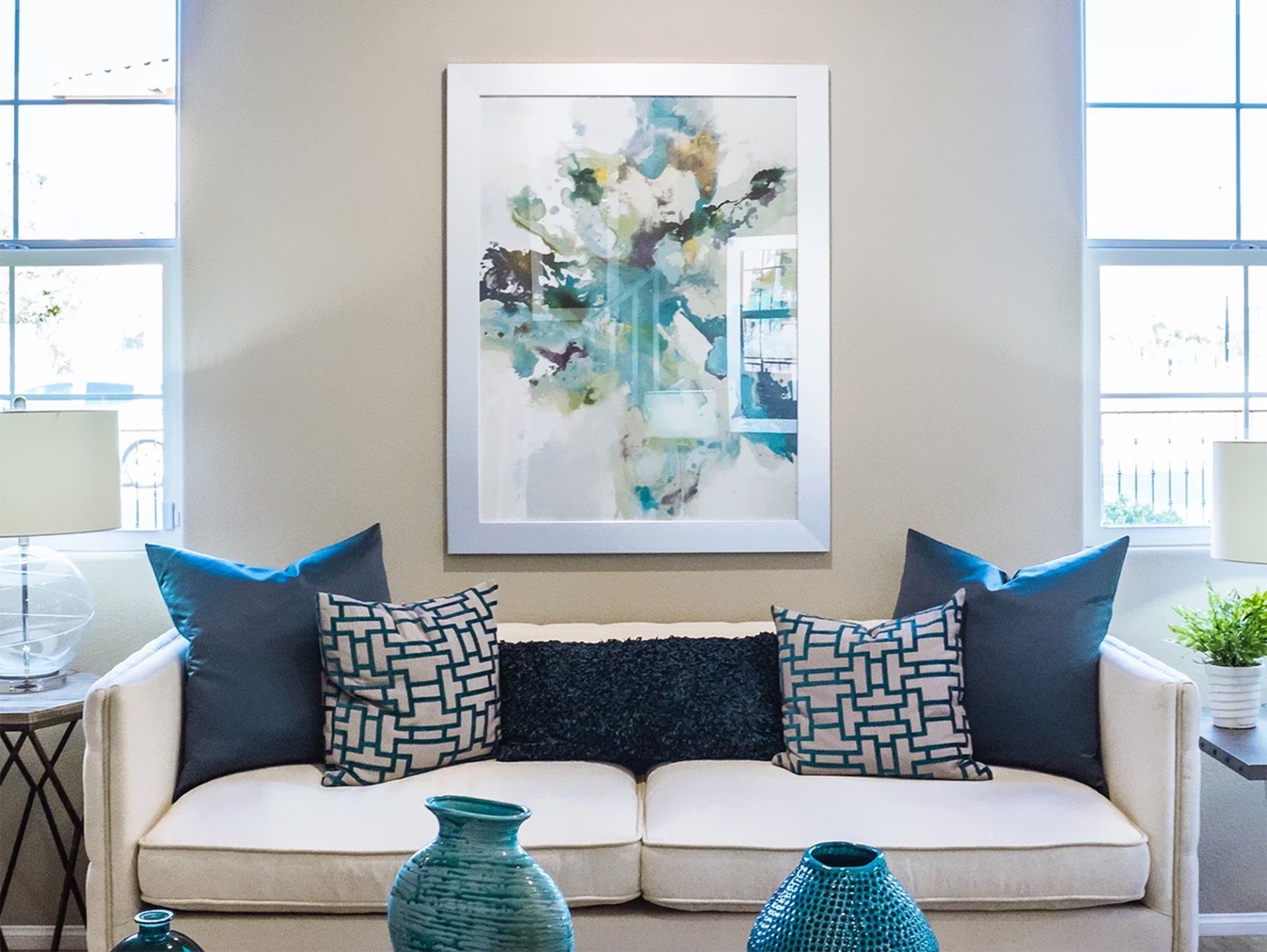 A living room with a couch , vases and a painting on the wall.