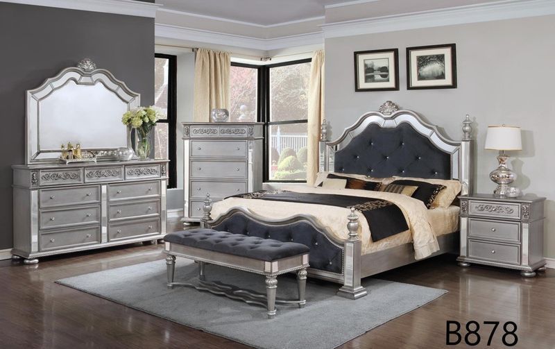 A bedroom with a bed , dresser , nightstand , mirror and bench.