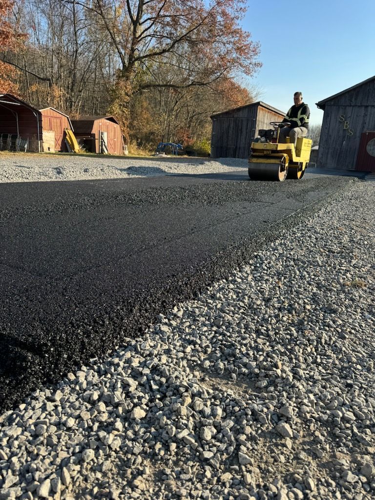 A man is driving a roller on a gravel road.