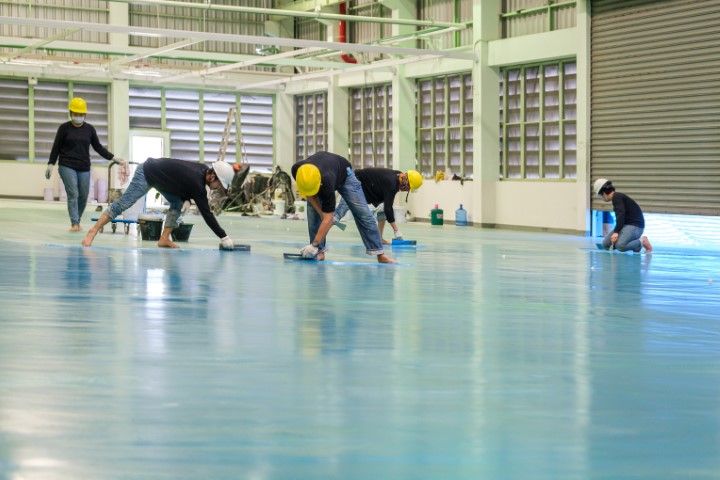 A group of people are cleaning a concrete floor in a warehouse.